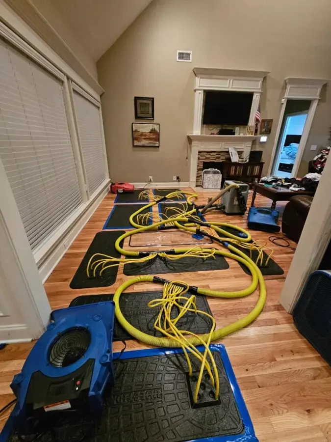 Hardwood drying mats with vacuum hoses laid across a living room floor