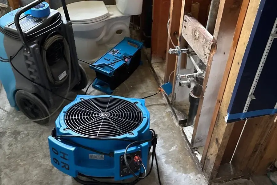 Dehumidifier and air mover drying an opened wall with exposed framing